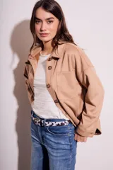 Sobrecamisa negra de estilo shacket, confeccionada en tejido de gamuza sintética. Presenta cuello camisero, cierre frontal de botones y dos bolsillos de parche con solapa en el pecho. El calce es oversize y las mangas son largas.