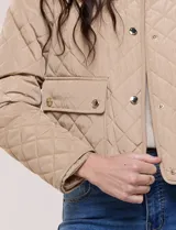 Campera corta capitoneada Michael Kors de color beige, con diseño acolchado en rombos, cuello camisero, cierre frontal de botones metálicos a presión y bolsillos frontales con solapa. Incluye un pequeño bolsillo en la manga.