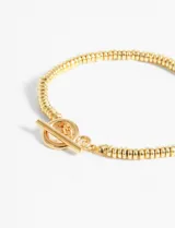 Pulsera dorada con cuentas tubulares y cierre de barra en forma de T.