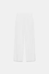 Pantalón blanco de tiro alto con corte ancho (palazzo o culotte), confeccionado en tejido con lino. Presenta pliegues marcados en la parte delantera y bolsillos laterales.