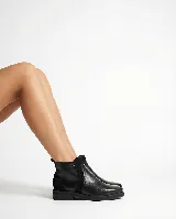 Bota corta tipo chelsea de cuero negro, con paneles laterales de gamuza y suela plana de goma. Presenta un diseño minimalista con tirador en la parte trasera.