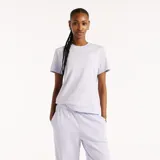Remera New Balance modelo Sport Essentials para mujer, de color lila con cuello redondo, mangas cortas y calce clásico. Presenta un pequeño logo de la marca bordado en el pecho.