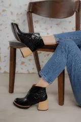 Bota corta de cuero vacuno con textura de reptil, color marrón oscuro. Cuenta con un taco cuadrado negro, suela de plataforma y una tira decorativa con hebilla metálica circular en el tobillo.