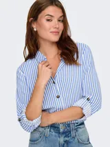 Camisa de corte suelto y textura fluida, con estampado de rayas verticales en azul y blanco. Presenta cuello camisero, cierre frontal de botones y mangas largas con opción de enrollado.