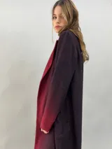 Tapado de paño de lana con diseño de solapas amplias, corte recto y bolsillos laterales ocultos. Presenta un degradado de color que va desde un tono bordó intenso en las solapas y puños hacia un tono más oscuro en el cuerpo.
