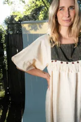 Túnica de lino color beige, de corte midi y diseño holgado, con mangas cortas y pechera combinada con tela estampada y detalles de flecos y botones.