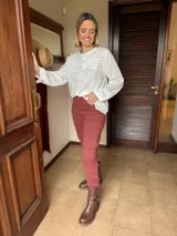 Camisa de lino color blanco con cuello redondo, cierre frontal de botones y detalle de alforzas y encaje en el pecho. Presenta mangas largas con puños abotonados y un corte recto.