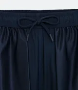 Bermuda deportiva gris con cintura elástica, cordón de ajuste, bolsillos con cremallera, recorte lateral con agujeritos y abertura en el bajo.