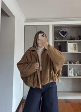 Campera tipo bomber de gamuza en color tostado, con diseño holgado, mangas amplias y cierre frontal con solapa.