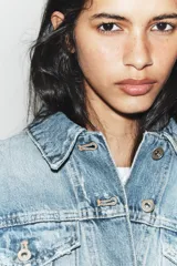 Cazadora de denim crop con cuello solapa, manga larga y cierre frontal con botones. Presenta efecto lavado, bolsillos de plastrón con solapa en el pecho y detalles de rotos.