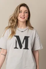 Remera gris con estampa de la letra M en negro y cadena plateada en el cuello.