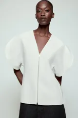 Top de Zara Woman Collection color blanco, con escote en pico, mangas cortas abullonadas con aberturas y cierre frontal con cremallera.