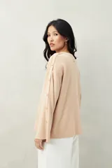 Sweater de tejido de punto color blanco hueso, con cuello redondo y mangas acampanadas. Presenta una hilera de botones a tono en el lateral de cada manga.