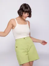 Bermuda de algodón color verde lima, de corte recto y tiro alto. Presenta cierre frontal con botones veteados, bolsillos laterales y elástico en la pretina trasera para mayor ajuste.