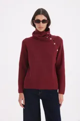 Sweater de punto en color bordó, con cuello alto tipo polera y cierre lateral mediante botones dorados. Presenta mangas largas y un diseño de tejido acanalado.