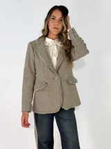 Blazer de corte clásico con textura de tejido de punto, color beige con detalles moteados. Presenta solapas tradicionales, cierre frontal de un botón, bolsillos laterales con solapa y bordes con acabado desflecado.