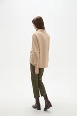 Blusa holgada de poliéster color beige, con cuello camisero, escote en V con botones frontales y mangas largas.