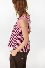 Musculosa de corte holgado con diseño a rayas horizontales en tonos marrón y crudo. Presenta ribetes en color fucsia en el cuello redondo y en las sisas, además de un pequeño bordado decorativo en el centro del pecho.