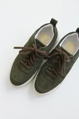 Zapatillas de gamuza verde oliva con cordones marrones y suela de goma color crema.