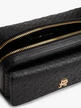 Cartera estilo camera bag negra, estructurada y compacta, con textura integral de monograma TH en relieve y placa metálica dorada con el logo TH en el frente. Posee cierre superior y correa ajustable para llevar al hombro o cruzada.