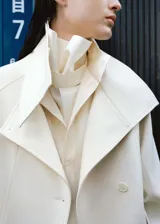 Parka de corte recto color blanco, confeccionada en mezcla de lana, con cuello embudo, bolsillos de solapa laterales, manga larga con trabillas y cierre delantero con botones.