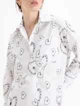 Camisa de poplin blanca con rayas verticales y estampado de corazones formados por cadenas, corte holgado, cuello clásico, mangas largas y bolsillo aplicado en el frente.