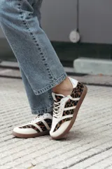 Zapatillas de estilo retro con diseño de paneles, combinando cuero beige con estampado animal print de leopardo y detalles en blanco. Presentan suela de goma color caramelo y cierre con cordones.