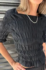 Remera negra de algodón con textura fruncida en todo el cuerpo y mangas cortas con terminación de volado.