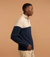 Buzo de media malla con diseño de bloques de color, presentando la parte superior en beige y la inferior en azul marino, separadas por una línea blanca. Cuenta con cuello alto con cierre frontal parcial y puños acanalados.