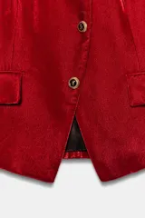 Blazer de terciopelo color rojo, con cuello subido, manga larga y cierre frontal cruzado con botones dorados. Presenta bolsillos delanteros con solapa.