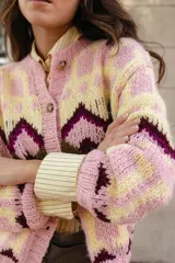 Saco tejido a mano con diseño jacquard geométrico en tonos rosa, amarillo y bordó. Presenta cuello a la base, cierre frontal con botones y silueta corta.