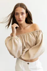 Blusa color beige de lino, con escote elastizado que permite usarla con los hombros descubiertos, mangas largas abullonadas con puños elastizados y corte crop.