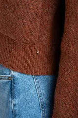 Cardigan de lana color marrón, con cuello alto, cierre frontal de botones y dos bolsillos delanteros. Presenta puños y ruedo acanalados.