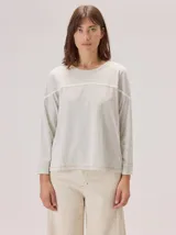 Remera de manga larga en color gris melange, con cuello redondo y detalle de costura horizontal a la altura del pecho. Presenta un diseño holgado y casual.