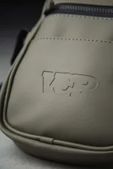 Mini morral de material engomado color verde militar, con compartimento principal y un bolsillo frontal con cierre negro. Cuenta con el logotipo de la marca grabado en relieve en la parte inferior y correa ajustable.