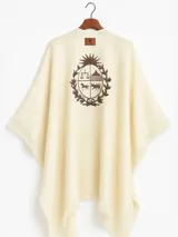 Ruana color crema con flecos y estampado del escudo de Uruguay en la espalda.
