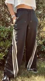 Pantalón deportivo color naranja con las icónicas tres rayas blancas laterales características de la marca Adidas.