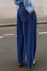 Jeans de tiro alto con corte loose fit y pernera holgada. Presenta detalle de corchetes en la cintura, bolsillos frontales y bolsillos de plastrón en la parte trasera. Cierre frontal con cremallera y botón.