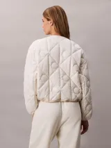 Campera puffer Calvin Klein color beige, de cuello redondo, manga larga y cierre frontal con cremallera blanca. Presenta bolsillos laterales y un parche con logo bordado en el pecho.