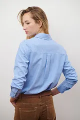 Camisa de corte recto confeccionada en tela Oxford, color azul claro. Presenta cuello clásico, cierre frontal con botones, mangas largas con puños abotonados y un bolsillo aplicado en el pecho.