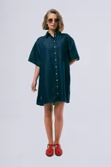 Vestido corto de denim azul oscuro, con cuello camisero, mangas cortas, cierre frontal con botones, bolsillo aplicado en el pecho y calce holgado.
