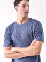 Remera de manga corta color gris topo, corte slim, con cuello redondo y un estampado gráfico en el pecho que combina texto manuscrito con un diseño abstracto en tonos oscuros.