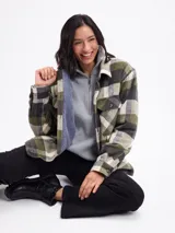 Sobrecamisa de corte holgado con estampado de cuadros en tonos verdes, beige y negro. Presenta cuello clásico, cierre frontal con botones, bolsillos en el pecho y un interior forrado en tejido sherpa de color azul.