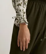 Blusa de crepé color blanco con estampado de hojas verdes, escote en V y mangas largas abullonadas con detalle de nudo en los puños.