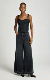 Jean wide leg negro de tiro alto con perneras anchas y dobladillo deshilachado, con bolsillos delanteros y traseros, y cierre frontal con botón metálico y cremallera.