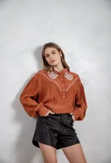 Camisa de manga larga color terracota con detalles bordados en hilo blanco en la parte frontal y hombros, escote en V y cierre frontal de botones.