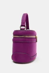 Bolso tipo vanity de estructura rígida en color fucsia, con acabado aterciopelado. Presenta un asa de mano superior, cierre de cremallera metálica dorada con doble tirador y correa bandolera ajustable y extraíble.