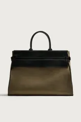 Bolso shopper de mano combinando cuerpo de gamuza color verde militar con solapa superior, asas y detalles en cuero sintético negro. Cuenta con compartimento principal con cierre imantado, bolsillo interior con cierre y bolsillo frontal plano con solapa.