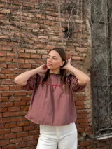 Blusa color chocolate con mangas cortas abullonadas, cuello redondo con volados y detalles de costura en zigzag de color rojo en el pecho y volados oscuros en los hombros.