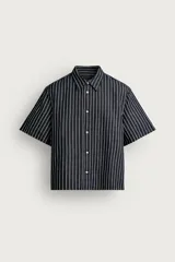 Camisa de corte relajado confeccionada en denim de algodón y lino, con diseño de rayas verticales, cuello solapa y manga corta con cierre frontal de botones.